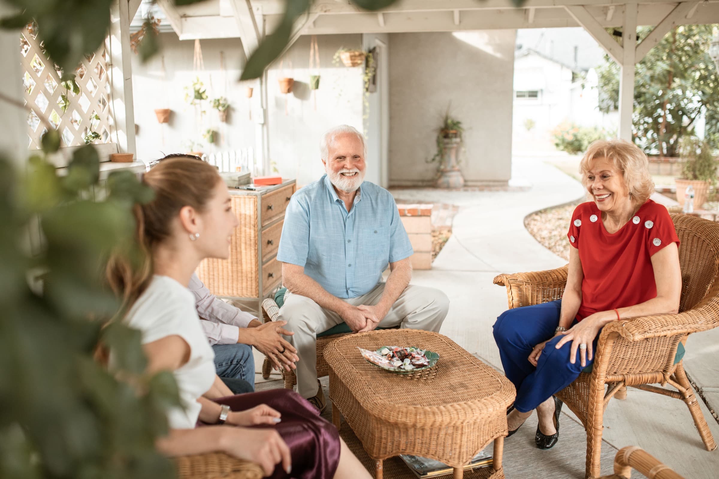 Three generations of a family sitting together on a bright porch, mid-conversation and at ease